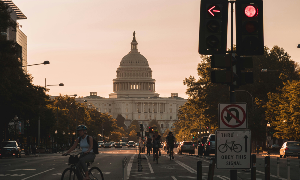 Image of Pennsylvania Ave, Washington, with traffic signals and cyclists in front of The Capitol.