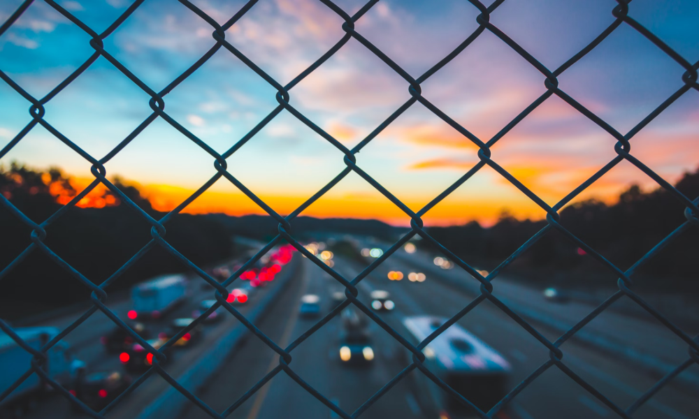 Picture of vehicles on a freeway taken from a bridge, viewed through a fence
